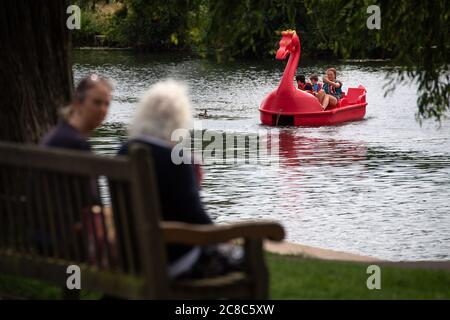 Friends have a conversation in St Nicholas' Park as a pedalo passes along the River Avon in Warwick, Warwickshire. Stock Photo