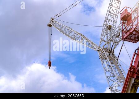 Crawler crane against blue sky and white clouds. Real estate industry. Red-white crane use reel lift up equipment in construction site. Crane for rent Stock Photo