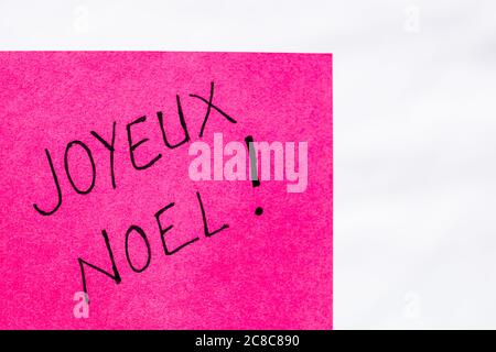 Joyeux noel (Merry Christmas) handwriting text close up isolated on pink paper with copy space. Writing text on memo post reminder Stock Photo