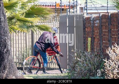 Alberton, South Africa - unidentified postman delivers mail by bicycle to houses in a residential neighbourhood image in horizontal format Stock Photo