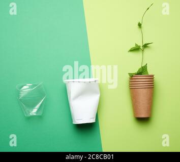 plastic drink cups and paper cup with branch and green leaves on green background, environmental pollution concept, no plastic, top view Stock Photo