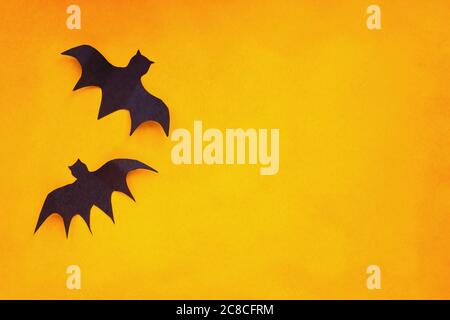 Halloween holiday decorations of two paper bats flying over an empty orange background with free space for text. Stock Photo