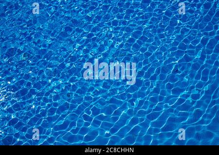 Swimming pool, blue clear water in the outdoor pool, with sun flare on the surface. Background of blue water in the pool. Ripples on the surface of th Stock Photo