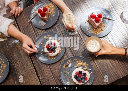 Bachelorette party, girls hands with drinks and sweet cakes with summer berries on a wooden table. Party, sweet table. Summer offer desserts in the re Stock Photo