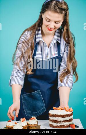 White happy long-haired woman with headband decorating cake with fresh berries in studio Stock Photo