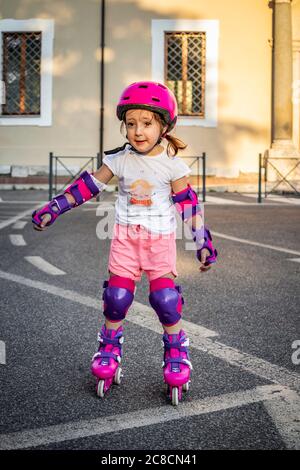 A little girl (child) learns to rollerblade on the street in the city. Safe with helmet and protections for elbows, wrists and knees. Concepts: fun, s Stock Photo