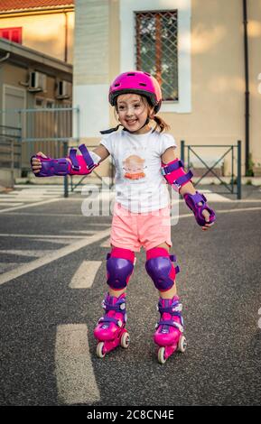 A little girl (child) learns to rollerblade on the street in the city. Safe with helmet and protections for elbows, wrists and knees. Concepts: fun, s Stock Photo