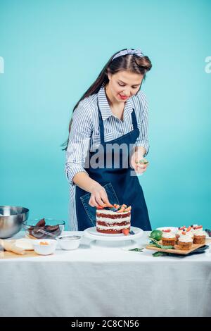 Caucasian hairstyled woman decorating tasty cake with fresh berries in studio Stock Photo