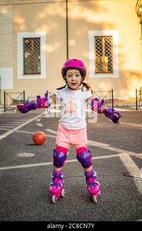 A little girl (child) learns to rollerblade on the street in the city. Safe with helmet and protections for elbows, wrists and knees. Concepts: fun, s Stock Photo