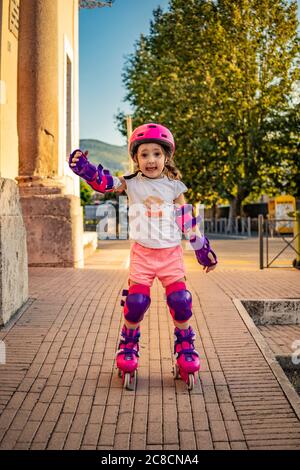 A little girl (child) learns to rollerblade on the street in the city. Safe with helmet and protections for elbows, wrists and knees. Concepts: fun, s Stock Photo