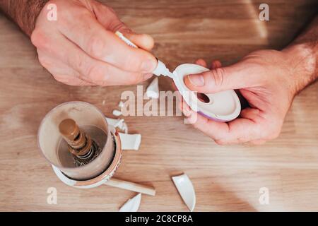 Male hands glue together fragments of ceramic dishes - superglue for repairing hard materials Stock Photo