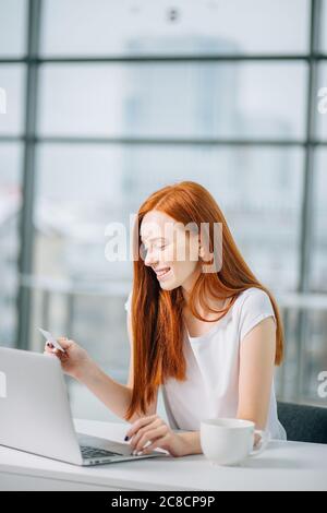 Close up of a happy redhead woman hand buying online with a laptop and paying with a credit card Stock Photo