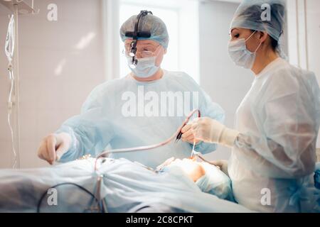 Nurse hand taking surgical instrument for group of surgeons at background operating patient in surgical theatre. Steel medical instruments ready to be Stock Photo