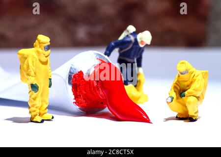 Miniature figure people wearing hazmat suits investigating a paint spill from an artists tube of acrylic paint Stock Photo