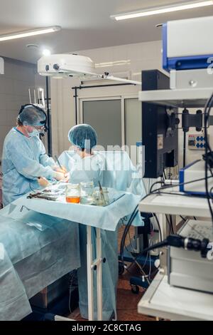 Wide view of a team of four surgeons operating on a patient in a dark OR at a hospital Stock Photo