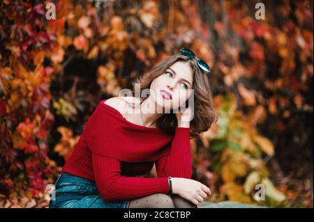 Beautiful young casual woman in glasses siting among yellow and red leaves in public park, Autumn colors Background Stock Photo