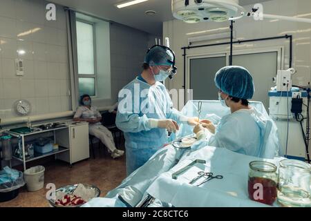 Wide view of a team of four surgeons operating on a patient in a dark OR at a hospital Stock Photo