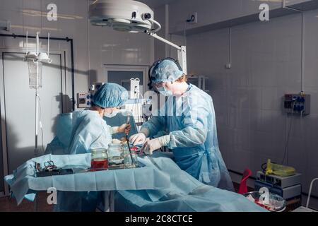 Wide view of a team of four surgeons operating on a patient in a dark OR at a hospital Stock Photo