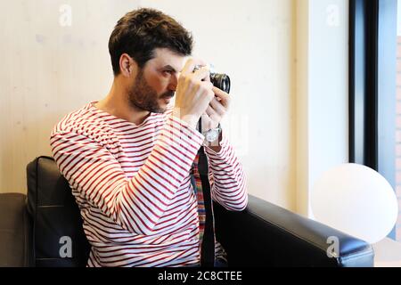 Bearded traveler male sitting on armchair while using a camera Stock Photo