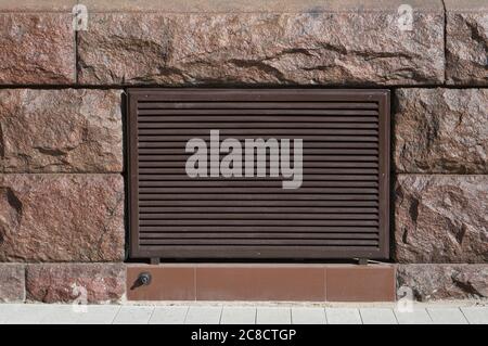 Metal grille of a ventilation shaft in a wall made of  granite stones Stock Photo