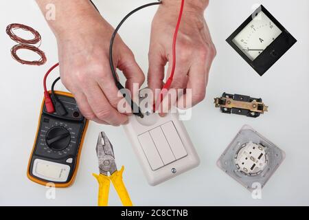 An home master checks the isolation of the light switch using a  multimeter Stock Photo