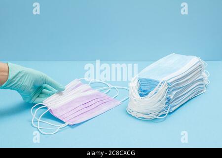 Doctor in a nitrile glove holding medical protective masks in her hand and a stack of masks on the blue background. Personal protective equipment agai Stock Photo