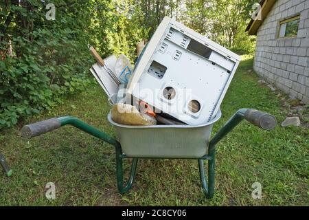 Great cleaning in a country house. Old rubbish and computer are taken out on a wheelbarrow. Summer day concept Stock Photo