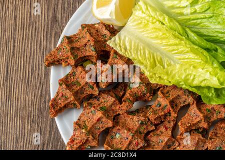 Cig kofte (raw meatball in Turkish) with lettuce and lemon. Turkish local raw food concept. Stock Photo