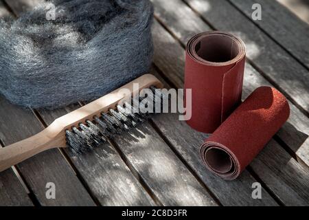 Wire brush and sandpaper lying on badly maintained wooden garden table before maintaining Stock Photo