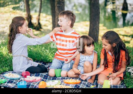 adorable little sibling kids eating in park outdoors. Feeding each other. Stock Photo