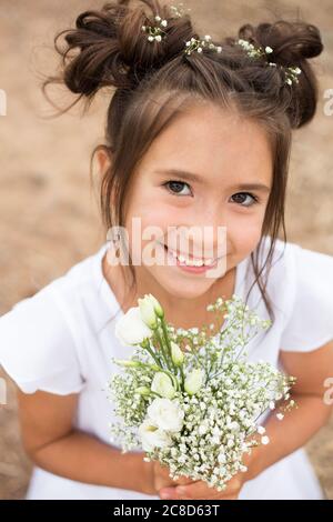 a child girl holds a bouquet of white flowers on a blurry background.dark hair , white flowers in her hands, white dress Stock Photo