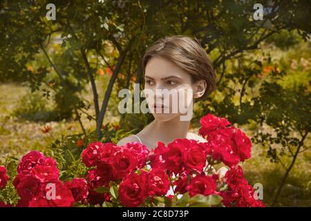 Beautiful girl with spring blooming red rose flowers. Stock Photo