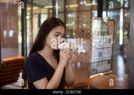 Long hair woman in dark blue dress sitting in the cafe waiting for her boyfriend, drinking hot coffee, hold a cup of coffee tightly. Stock Photo