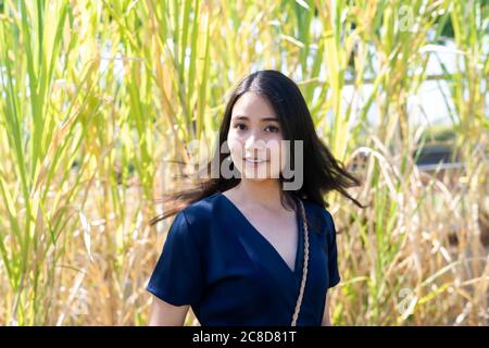 Long hair woman in dark blue dress flick her hair while standing in front of tall grass. Stock Photo