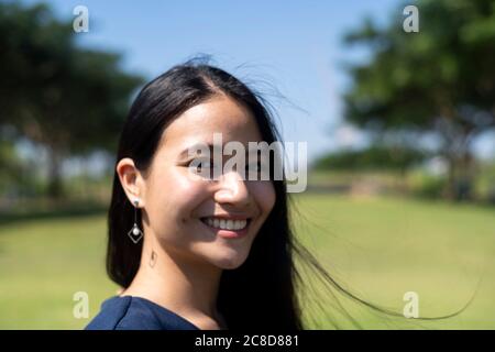 Long hair woman smile while standing on the grass field in the park in windy day and sunshine. Stock Photo