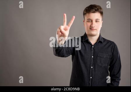 Portrait of serious stylish attractive man dressed with a casual black shirt showing peace gesture isolated on grey background with copy space adverti Stock Photo