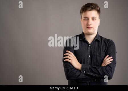 Portrait of serious stylish attractive man dressed with a casual black shirt standing with arms crossed isolated on grey background with copy space ad Stock Photo