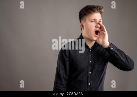 Portrait of serious stylish attractive man dressed with a casual black shirt shouting with his hand to his mouth posing on isolated black background w Stock Photo
