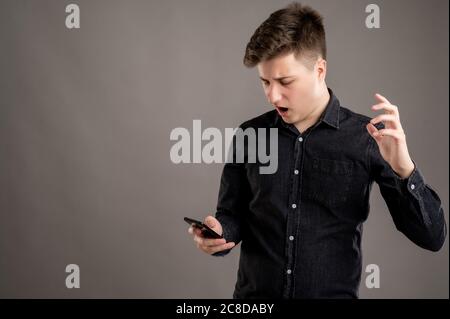Portrait of serious stylish attractive man dressed with a casual black shirt using mobile applications text messages gesturing angry face on cellphone Stock Photo
