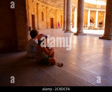 Granada, Spain 07/13/2010: Two tired school age kids are resting on a step in the palace of Charles V building in Alhambra Palace. The exhausted child Stock Photo