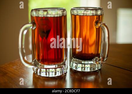 Close up image of two large glass beer mugs filled with fresh black tea. Mugs are sitting on an open window sill with trees in the background. Stock Photo