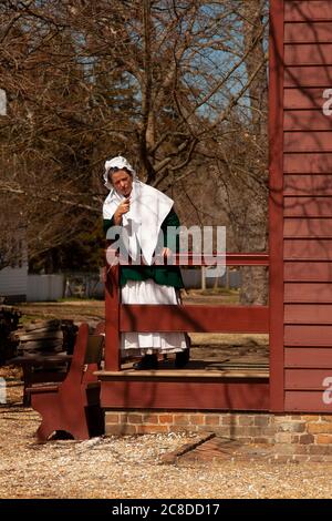 Williamsburg, Virgina, USA 02/22/2014:  Portrait of a white colonial woman standing by the railings of her historic farm house pointing at something. Stock Photo