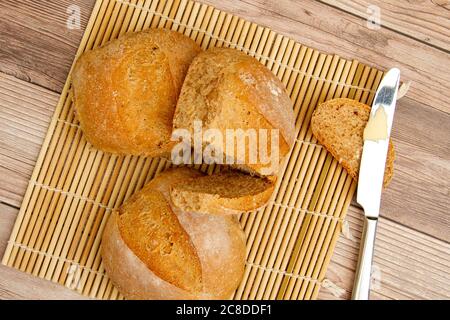 close up image of home made whole wheat bread loaves fresh out of oven. They are cooling on a bamboo mat on wooden table. A butter knife with butter. Stock Photo