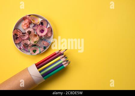Color pencils in paper packaging tube and shavings on bright yellow background, mockup and copyspace for text. Back to school or training classes Stock Photo