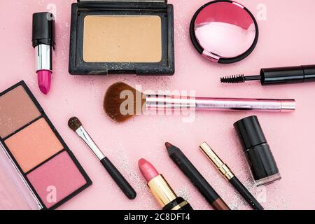 Make up cosmetics festive flat lay. Lipstick and nail polish, eye shadows and blush, brushes and pencils against pink glitter background Stock Photo