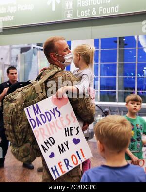 MSgt. Bryce Weight, an Alaska Air Guardsmen with the 176th Security Forces Squadron, holds his daughter with her welcome home sign in hand, at Ted Stevens-Anchorage International Airport upon his return from Kandahar, Afghanistan on June 22, 2020. 12 AKNG Airmen deployed in support of Operation Freedom Sentinel, a NATO-led continuation of the Global War on Terrorism. (U.S. Air National Guard photo by Lt. Col. Candis Olmstead/Released) Stock Photo