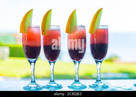 Row of glasses with natural juice decorated with melon on the bar. Blue sea on the background. Summer luxury tropical restaurant. Elegant cocktails se Stock Photo