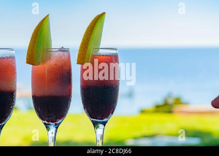 Row of glasses with natural juice decorated with melon on the bar. Blue sea on the background. Summer luxury tropical restaurant. Elegant cocktails se Stock Photo