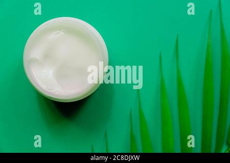 White jar of face cream on a background of tropical palm green leaf. blue background, top view, flat lay. Concept of natural cosmetics