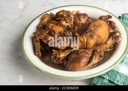 A serving of Filipino-style chicken adobo dish in a bowl with green napkin set on a marble tabletop. Stock Photo